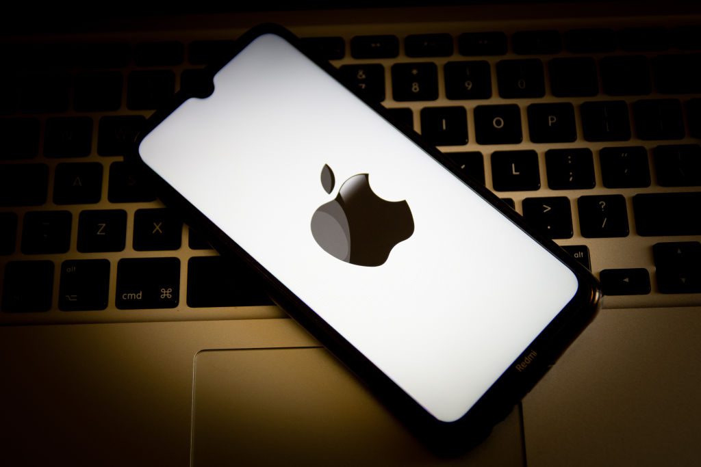 In this photo illustration, an Apple logo seen displayed on a smartphone screen with a computer keyboard in the background.