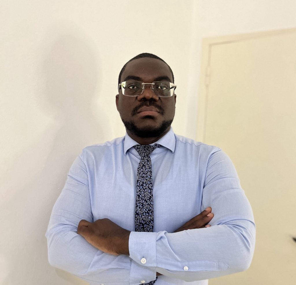 Teixeira Cândido stands with arms folded across his chest. He is wearing glasses, and a blue shirt with a tie.