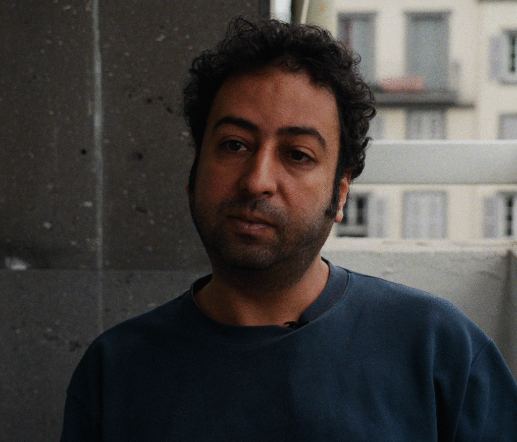 Photo of Omar Radi. He has dark curly hair and facial hair. He wears a blue sweatshirt.