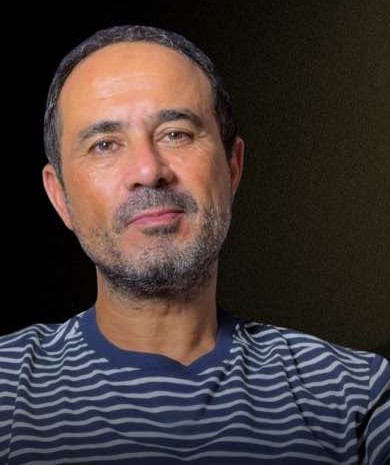 Photo of Soulaiman Raissouni, looking towards the camera. He has brown eyes, short hair, and facial hair. He wears a striped shirt.