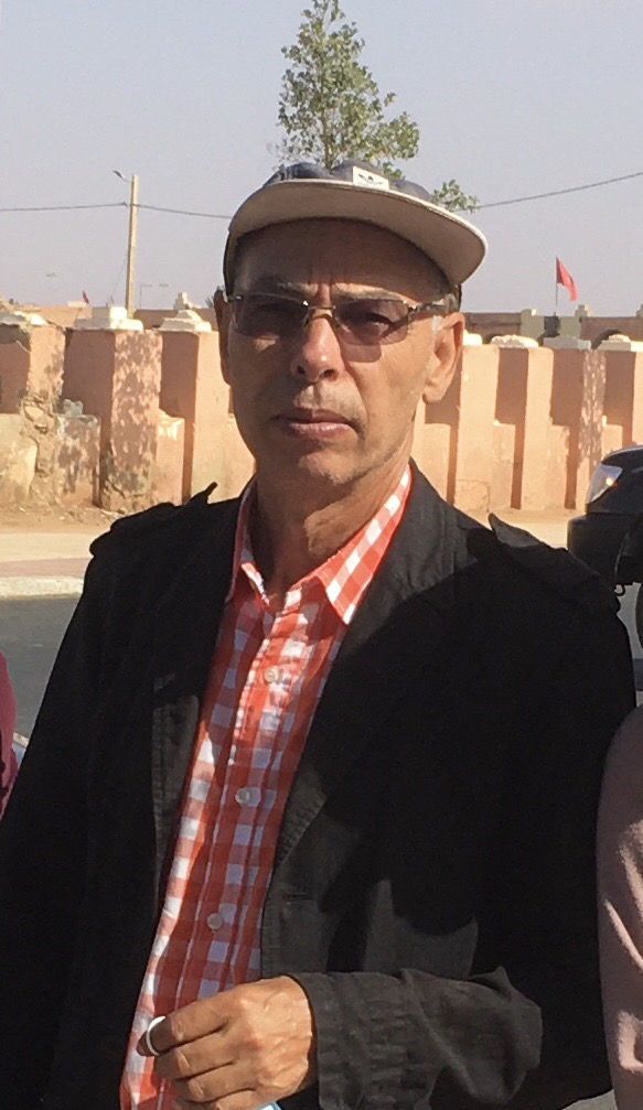 Photo of Maâti Monjib standing looking towards the camera. He wears sunglasses, a cap and a shirt.